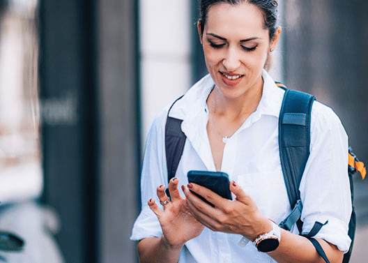 Woman Walking Outside with Backpack while Staying Connected to Work on Mobile Phone - iTacit