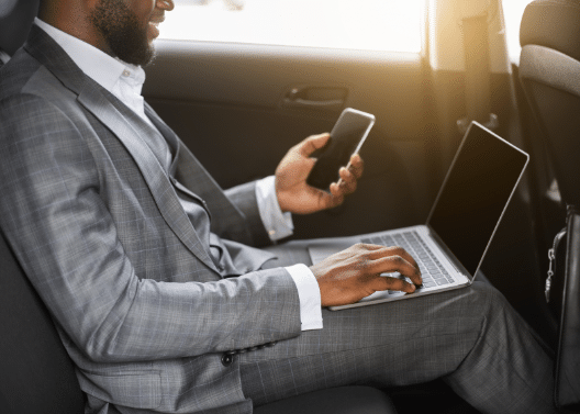 Man in Suit in Back of Car Staying Connected to Work on Laptop and Mobile Phone - iTacit