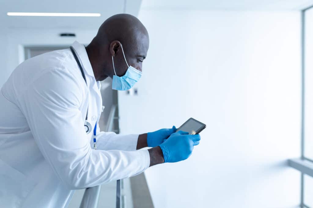 Male Frontline Healthcare Worker Standing against Railing Using Tablet - iTacit