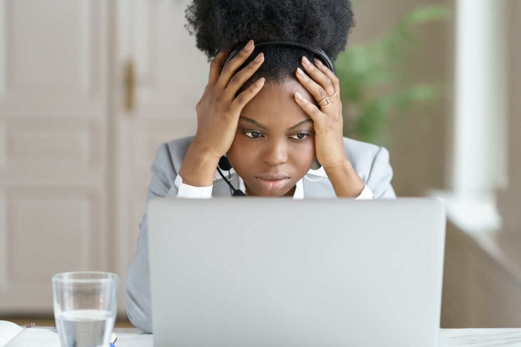 Woman Working on Laptop Wearing Headset Looking Distressed with Face in Hands - iTacit