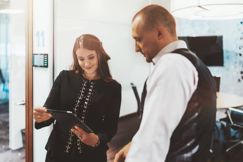 Woman and Man Coworkers Standing Together Talking While Looking at Tablet