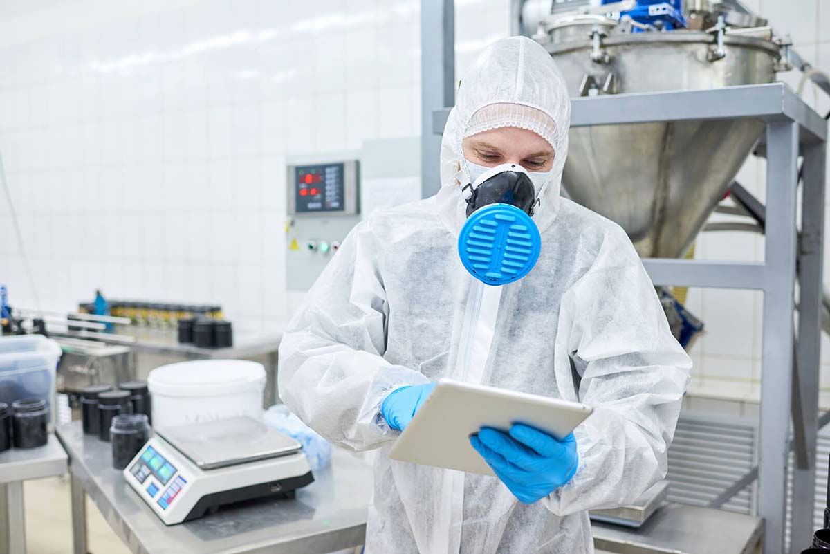 Factory Worker Wearing Safety Suit and Breathing Mask while Using Tablet